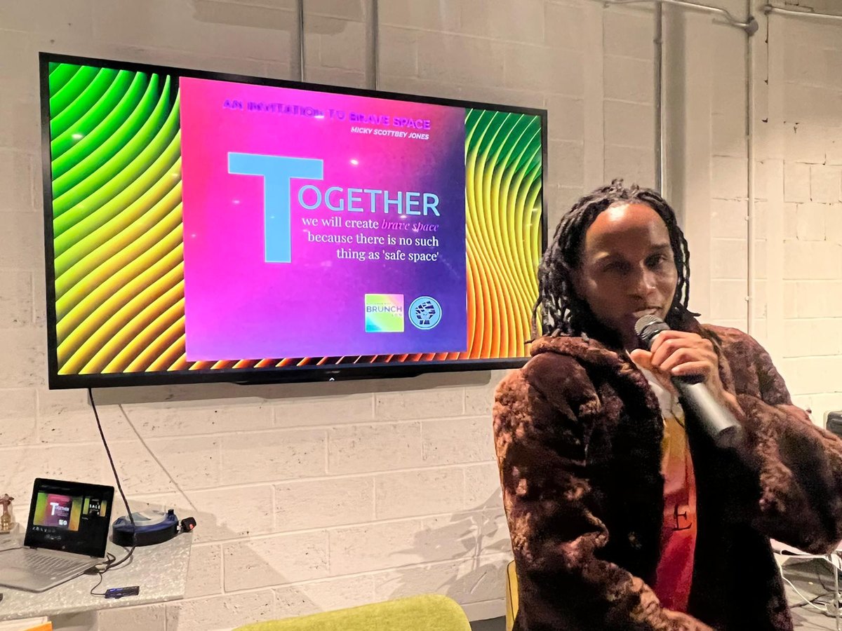 A member speaking beneath a screen reading: together we will create brave space